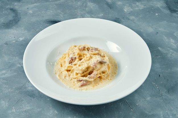 Massa italiana à carbonara com molho branco, parmesão e bacon em prato branco. Espaguete caseiro