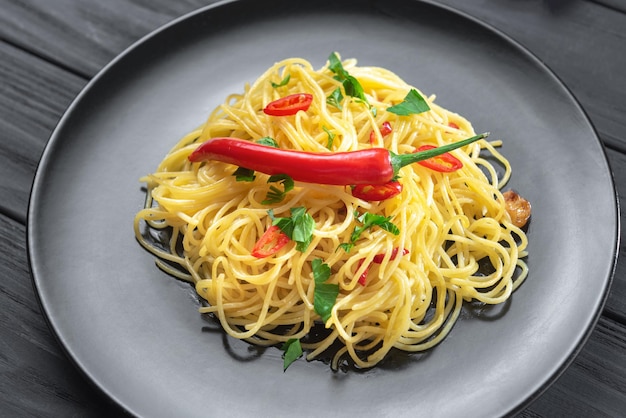 Massa italiana aglio olio e peperoncino em uma placa preta em um fundo escuro de madeira