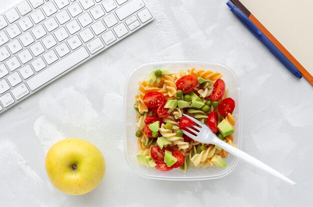 Massa italiana com legumes na mesa de escritório com teclado