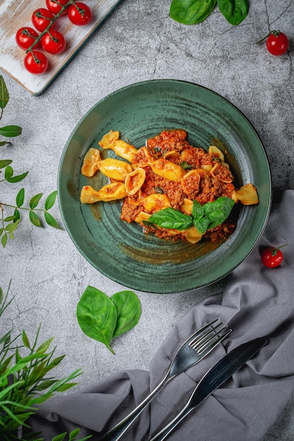 Massa italiana Conchiglioni Rigati recheada com tomate seco e carne com manjericão e queijo em uma mesa de pedra cinza. Cardápio do restaurante