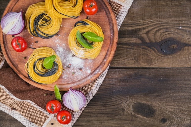 Massa italiana crua com ingredientes. tomate cereja, espaguete cru, cebola roxa e ervas em uma mesa de madeira rústica escura. conceito de cozinha. vista superior com espaço de cópia para o texto