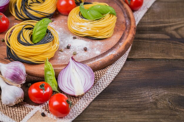 Massa italiana crua com ingredientes. Tomate cereja, espaguete cru, cebola roxa e ervas em uma mesa de madeira rústica escura. Conceito de cozinha.