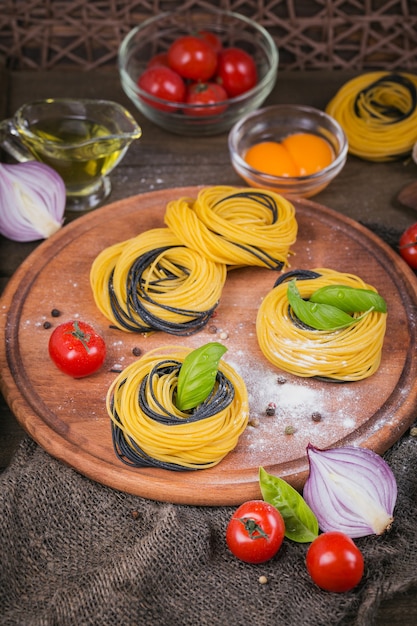 Massa italiana crua com ingredientes. Tomate cereja, espaguete cru, cebola roxa, ovos e ervas em uma mesa de madeira rústica escura. Conceito de cozinha.