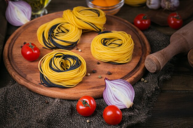 Massa italiana crua com ingredientes. Tomate cereja, espaguete cru, cebola roxa, ovos e ervas em uma mesa de madeira rústica escura. Conceito de cozinha.