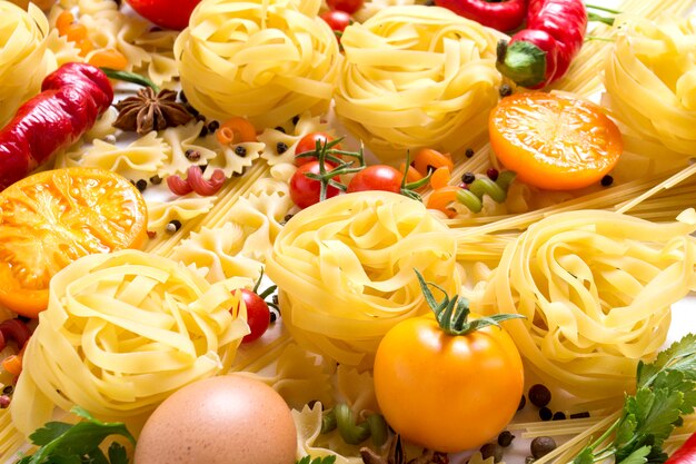 Massa italiana de vários tipos com especiarias, pimenta vermelha, ovos de galinha, tomates amarelos e vermelhos em um branco. conceito de cozinhar massas e molho italiano