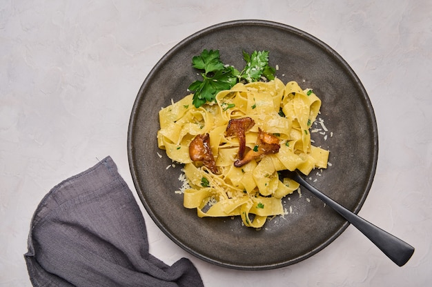 Massa italiana pappardelle com cogumelos chanterelles queijo e salsa no prato escuro com preto