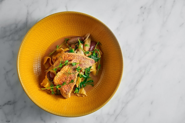 Massa pappardelle com salmonete frito, bárbula e microgrine em um prato amarelo brilhante sobre mármore branco