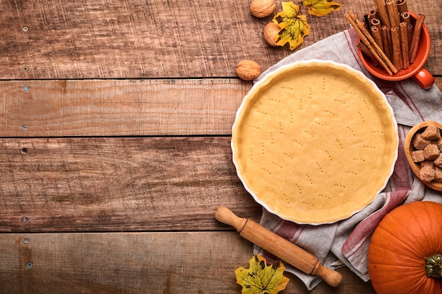 Massa para assar quiche, torta ou torta em forma de cozimento de cerâmica pronta para assar na toalha de cozinha sobre fundo de prancha rústica de madeira velha. Vista superior, copie o espaço. Cozimento caseiro de conceito para as férias.