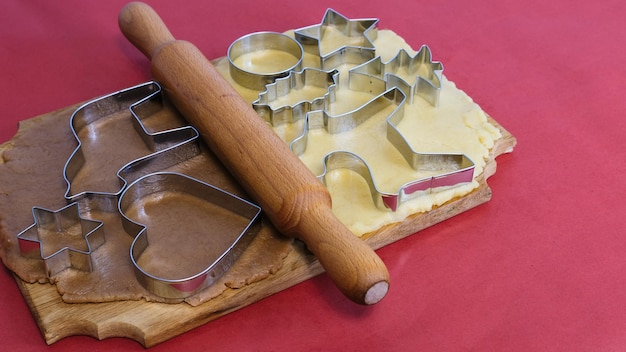 Massa para fazer biscoitos caseiros de gengibre em uma placa de madeira sobre um fundo vermelhoNatal e Ne