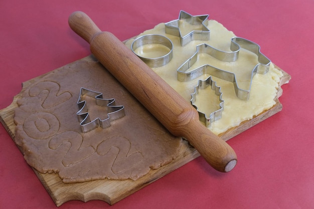 Massa para fazer biscoitos caseiros de gengibre em uma placa de madeira sobre um fundo vermelhoNatal