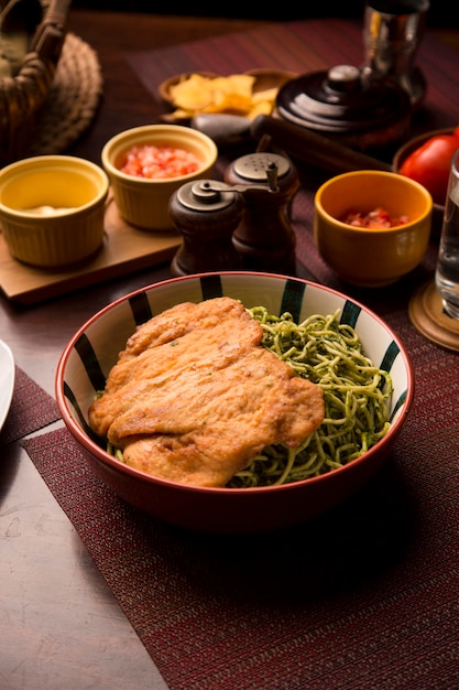 Massa verde pesto de frango à milanesa filé comida tradicional peruana mise en place mesa de madeira