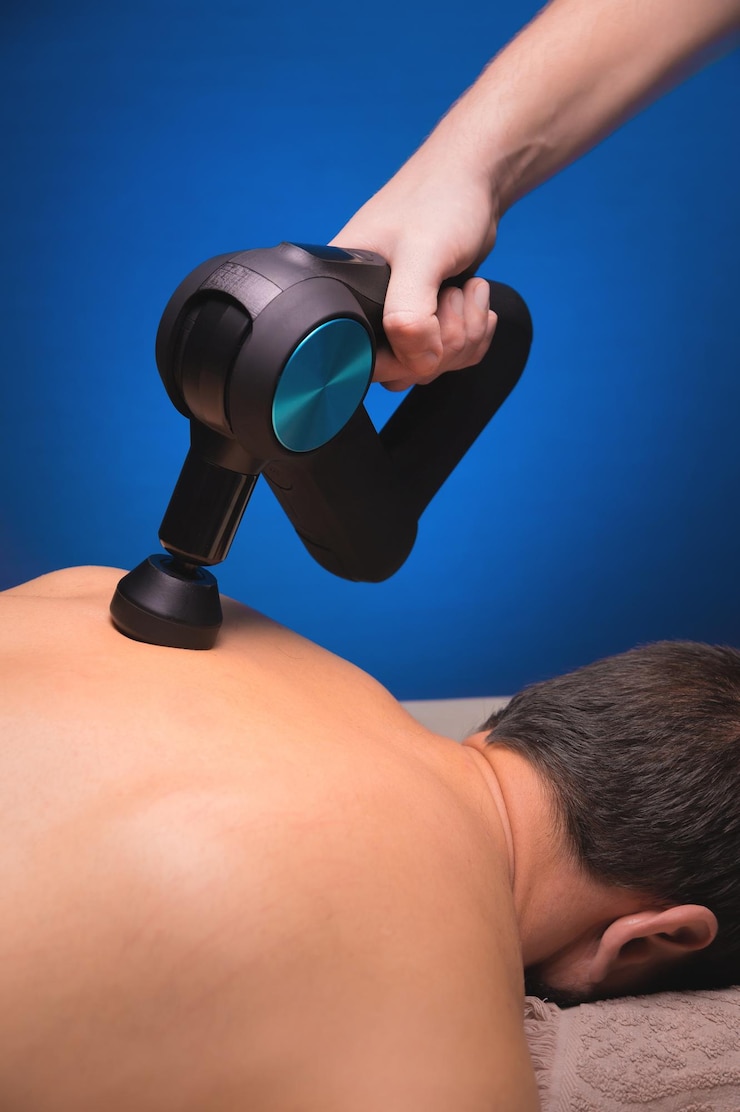 Foto massageador de percussão nas mãos de um massagista faz uma massagem dos ombros e parte superior das costas para um