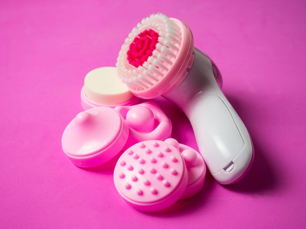 Massageador facial elétrico e bicos em um fundo rosa