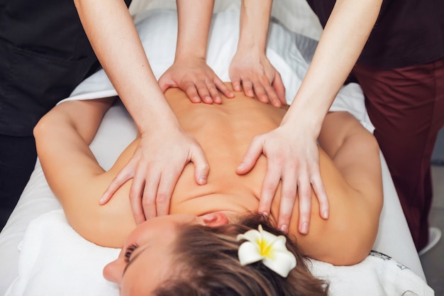 Massagem a quatro mãos em salão SPA. Dois massageadores fazem a massagem de volta para a mulher. Massagem tântrica sensual a 4 mãos de massagista profissional. Conceito de saúde e beleza feminina