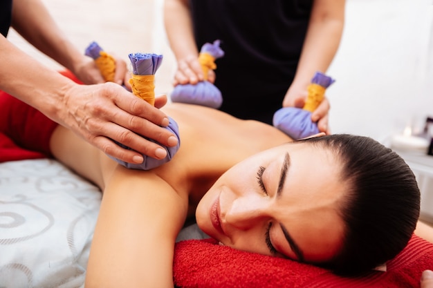 Massagem extraordinária. mulher agradável desfrutando de um tratamento gentil enquanto mestres acariciando seu corpo nu no gabinete do spa