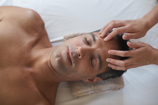 Massagem facial com as mãos e vista superior do homem no salão de cuidados com a pele paz e calma no resort de luxo na mesa para bem-estar acima da terapia e massagista no spa para tratamento da cabeça saúde e pessoa relaxar
