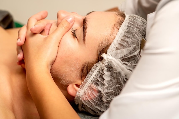 Massagem facial Linda jovem branca caucasiana tendo uma massagem facial com os olhos fechados em um salão de spa