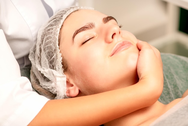 Massagem facial Mãos de um massagista massageando o pescoço de uma jovem caucasiana em um salão de spa o conceito de massagem de saúde