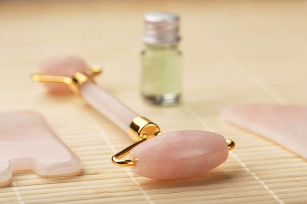 Massagem Gua sha feita de rolete de quartzo rosa natural, pedra jade e óleo, sobre um fundo de bambu para cuidados com o rosto e o corpo.