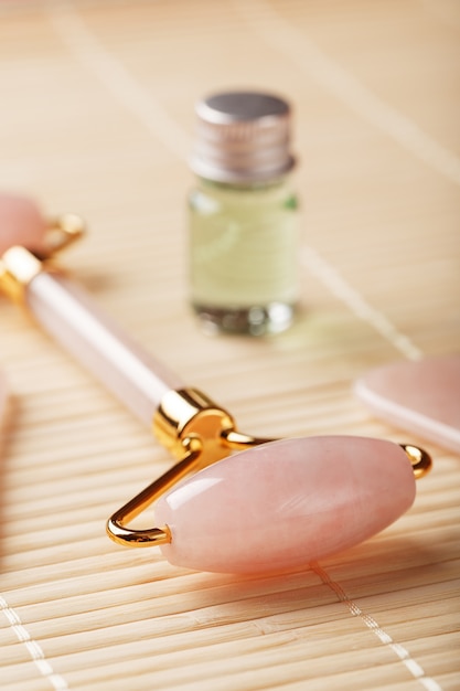 Massagem gua sha feita de rolete de quartzo rosa natural, pedra jade e óleo, sobre um fundo de bambu para cuidados com o rosto e o corpo.