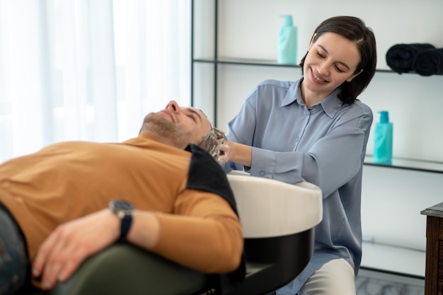 Foto massagem na cabeça. jovem sentado na cadeira enquanto faz massagem na cabeça e parece relaxado