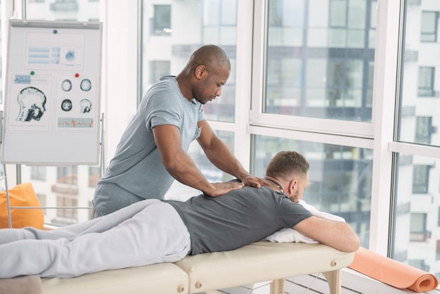 Massagem nas costas. Homem bom e forte perto de seu paciente enquanto massageia suas costas