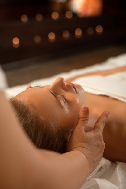 Massagem relaxante. Senhora atraente e impecável com cabelo preso dormindo durante massagem facial em um centro de spa profissional