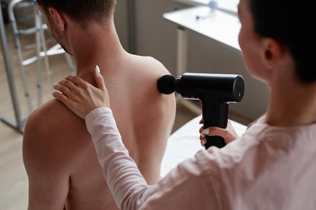 Foto massagetherapeut verwendet einen massagegerät zur behandlung von rückenschmerzen bei patienten im krankenhaus