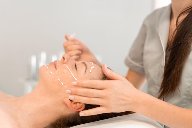 Massagista aplicando creme facial a uma mulher relaxada no salão