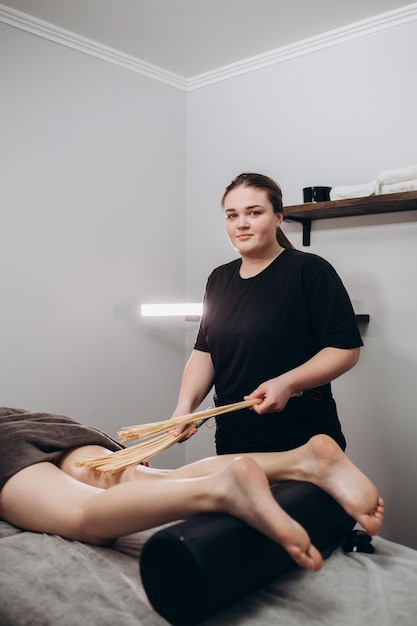 Massagista faz massagem para jovem Mulher fazendo massagem com bastão de bambu no spa diurno