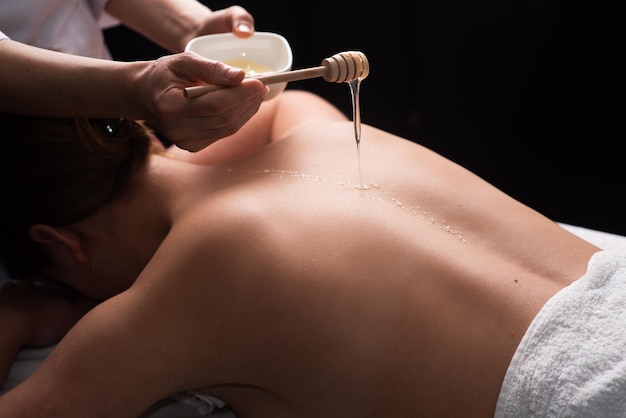Massagista fazendo massagem nas costas com mel no quarto escuro