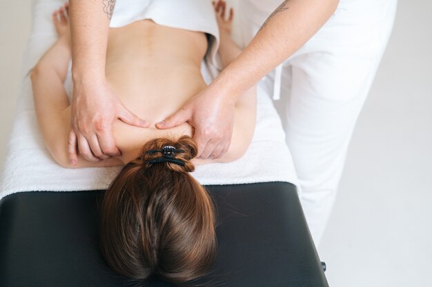 Massagista masculino com mãos fortes massageando profissionalmente as escápulas e os ombros de uma cliente