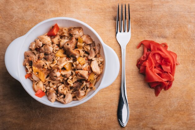 Massas asiáticas ou macarrão com legumes e carne com molho picante na placa de madeira com garfo