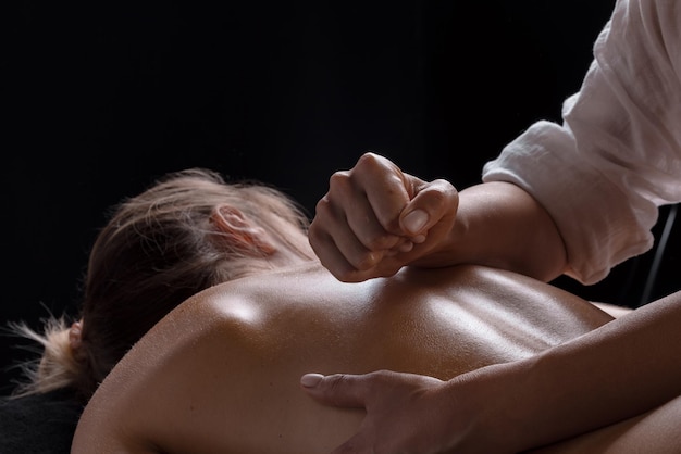 Masseurmädchen macht eine Massagenahaufnahme auf einem dunklen Hintergrund Nahaufnahmemassage