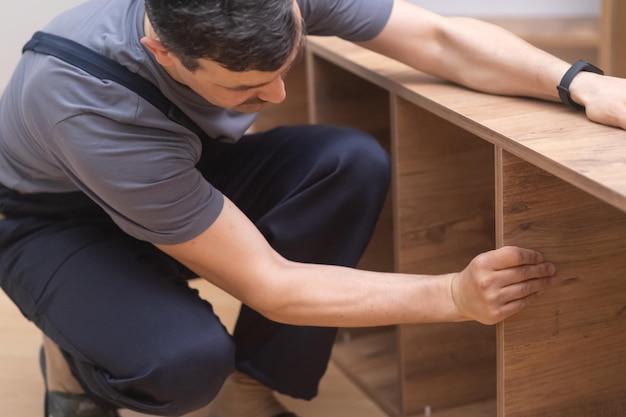 Maßgeschneiderte Möbelherstellung und Reparatur eines Mannes im Overall, der Regale auf einem Holzregal installiert