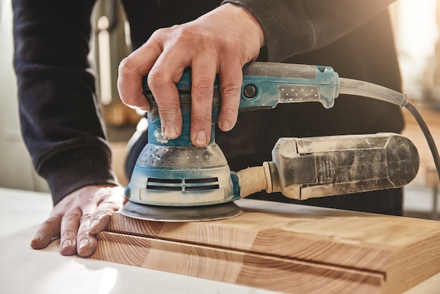 Foto massiv wie das holz, mit dem wir arbeiten, schleift der arbeiter das holz der winkelschleifmaschine