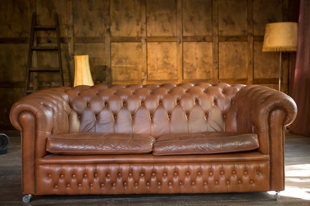 Massives Ledersofa in einem Holzinterieur. Braune Farbe Couch im Innen- oder Büro-Loft-Stil Interieur