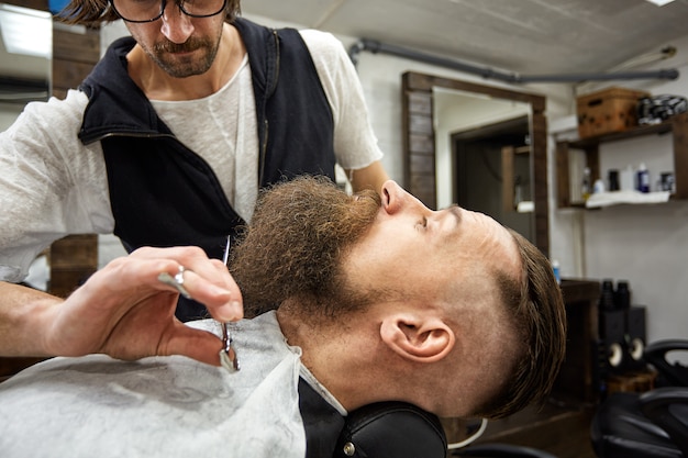 Master Barber macht Frisur und Styling. Konzept Barbershop. Bart Styling und Schnitt. Styling von schwarzem Bart. So trendy und stylisch. Werbe- und Friseurkonzept