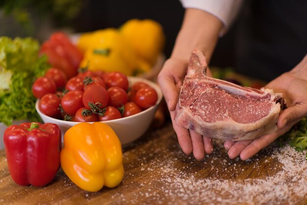 Foto master chef sosteniendo jugosa rebanada de bistec crudo con verduras alrededor de una mesa de madera