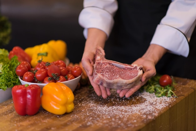 Master Chef sosteniendo jugosa rebanada de bistec crudo con verduras alrededor de una mesa de madera