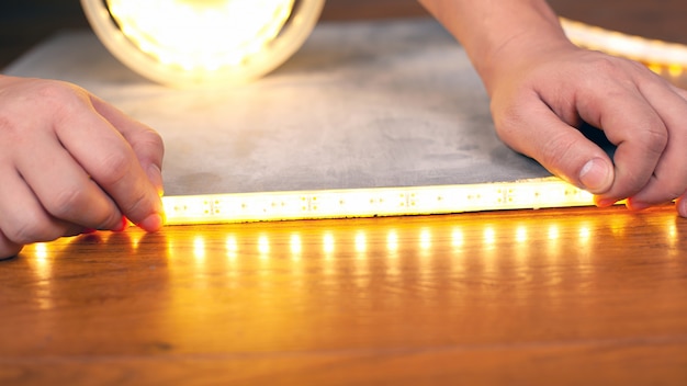 Master instala un primer plano luminoso de tira de led, cinta adhesiva de  manos sobre una superficie de madera.