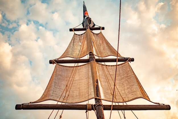 Foto mastro de navio com velas bege balançando contra o céu azul