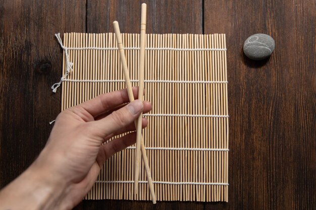 Mat y palillos de madera para rollos sobre un fondo de madera oscura.