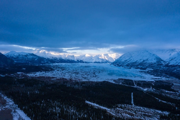 Matanuska-Gletscherterminus, schneebedeckte Berge und Wald an einem bewölkten Tag. Alaska, USA. Luftaufnahme