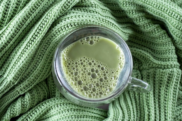 Matcha Green Tea Latte in einer klaren, herzförmigen Tasse auf grünem, gehäkeltem, kariertem Hintergrund