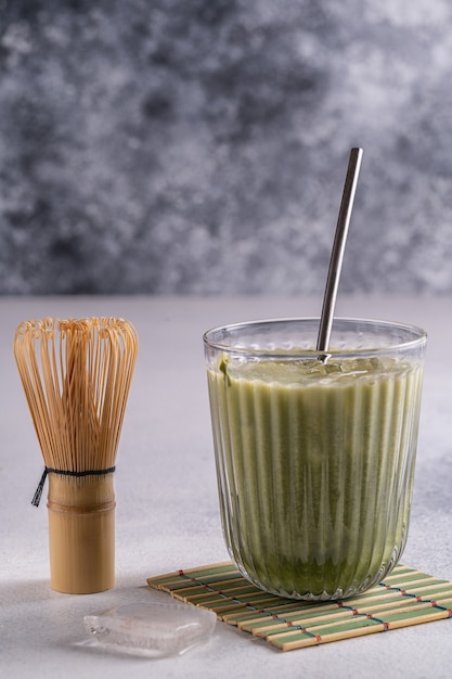 Matcha latte com espuma de creme em copos, tusaku de bambu e matcha em pó na mesa de madeira.