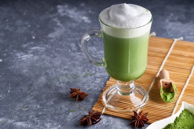 Matcha Latte com leite de amêndoa e creme em vidro na mesa de pedra cinza