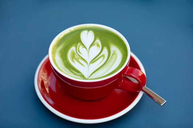 Matcha Latte grüner Milchschaum rote Tasse auf blauem Tisch im Café Trendiger Powertee-Trend aus Japan