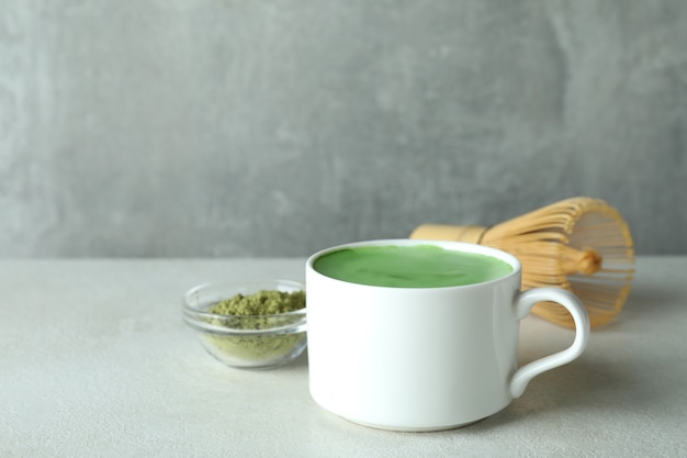 Matcha Latte und Zubehör für die Zubereitung auf weißem strukturiertem Tisch