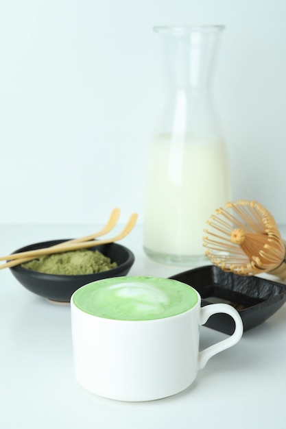 Matcha Latte und Zubehör für die Zubereitung auf weißem Tisch